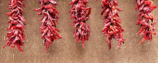 Hanging chili peppers ristras against adobe wall.