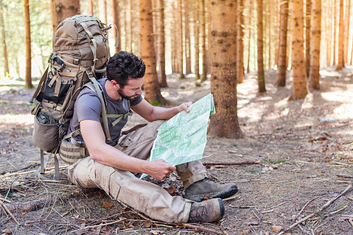 Beard Man with Backpack and map searching directions in wilderness area