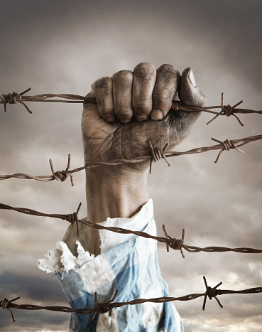 Hand of a refugee behind barbed wire