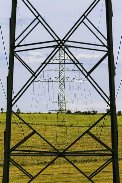 Electricity Pylon with blue sky and green field in background
