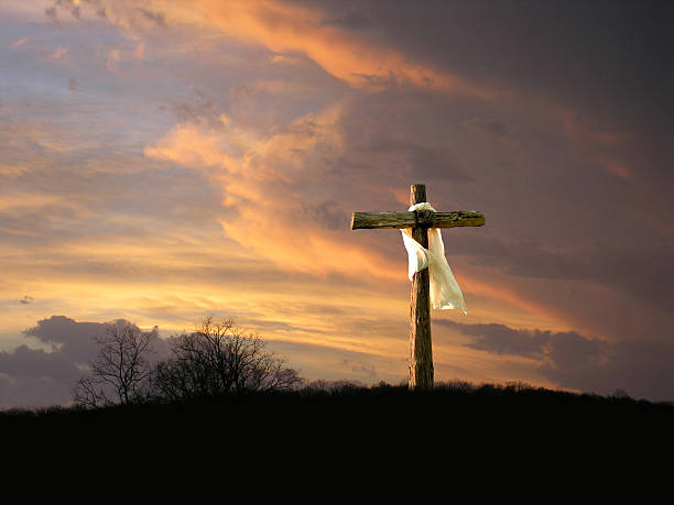 Cross with Sunrise The cross of Jesus Christ from the Bible. The garment is blowing in the wind, left to right, suggesting that the brighter skies on the left are coming soon. holy week photos stock pictures, royalty-free photos & images