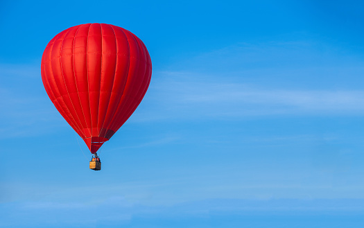 Red hot air balloon in blue sky with white clouds