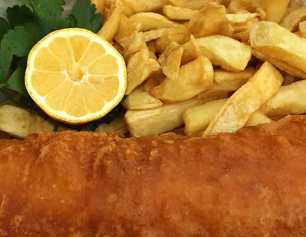 Photo showing a meal of takeaway cod and chips, which has just been purchased from a chip shop.  This 'fish supper' feels a little more of a gourmet meal, since it comes with a slice of lemon and a sprig of flat-leaf parsley.