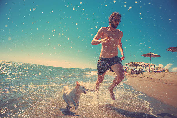 uomo che corre con il cane sulla spiaggia - cane al mare foto e immagini stock