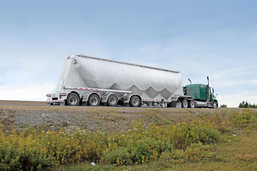 Rear quarter view of a semi truck hauling a pneumatic tank trailer, designed to carry vacuum sealed dry bulk cargo and emptying using a pump and compressed air. 