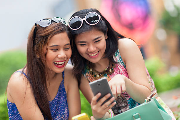 duas mulheres jovens se divertindo usando um smartphone - asian ethnicity philippines women beauty - fotografias e filmes do acervo