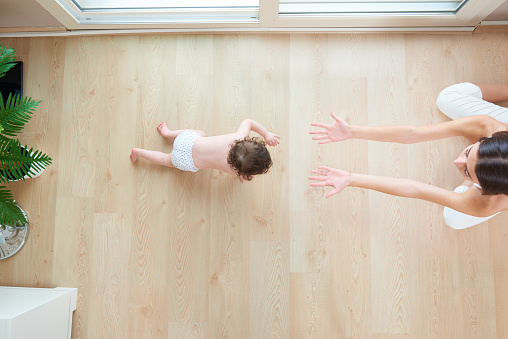 A top view of a baby girl crawling toward her mother