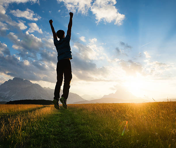 allegro uomo saltando su un prato al tramonto - arms raised green jumping hand raised foto e immagini stock