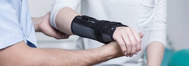 Contused hand in stabilizer Woman with dislocated wrist in stabilizer is consulting doctor orthopedics photos stock pictures, royalty-free photos & images