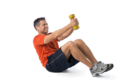 Mid adult man sitting on floor holding dumb bell doing ab exercise, isolated on white background