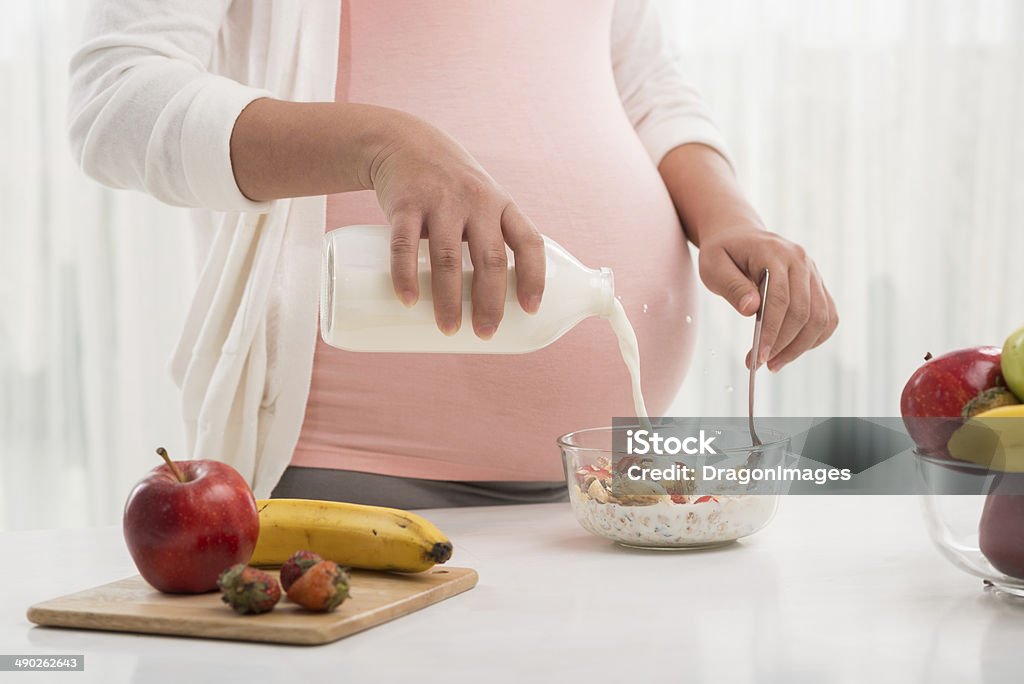 Healthy breakfast Pregnant woman pouring milk into her bowl with fruit fresh Pregnant Stock Photo