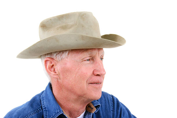 Portrait of senior adult cowboy on white background. He wears his favorite old, worn cowboy hat.