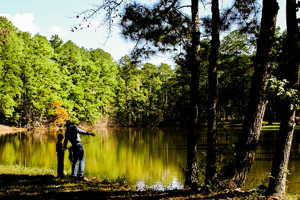 Senior grandfather teaches his grandson how to fish at their local pond.  Multi-generation family.