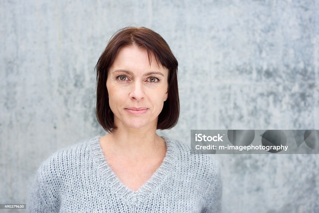 Older woman with brown hair Close up portrait of a beautiful older woman with brown hair standing against gray background Portrait Stock Photo
