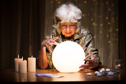 Fortune teller with Cristal ball on red velvet. Looking at Christal ball.