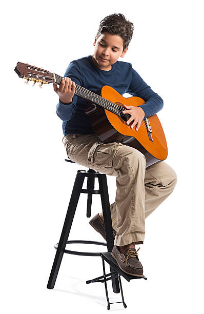 Child Playing Guitar on Chair Child on chair playing classical guitar isolated on white background. juvenile musician stock pictures, royalty-free photos & images