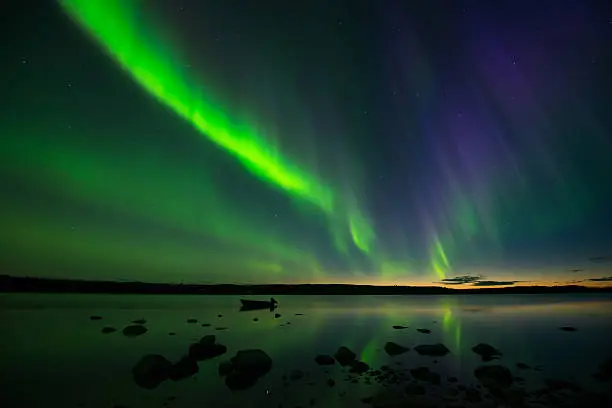 Colorful aurora borealis appear above a quiet lake and lit up the starry sky right after the sun sets.