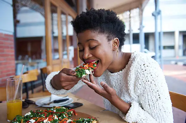 Photo of African american woman eating pizza at outdoor restaurant