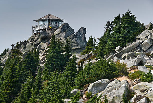 Mount Pilchuck Fire Lookout Mount Pilchuck State Park, Washington, USA - August 11, 2015: The historic Mount Pilchuck fire lookout was originally built in 1918 and rebuilt for visitor use in 1990. The lookout can be reached by hiking through beautiful old-growth forest and heather-covered meadows to the rocky summit.  There you can see an incredible panoramic view of the Puget Sound lowlands and the Cascade and Olympic Mountains.  These hikers were photographed standing on the fire lookout deck after reaching the 5341' summit of the mountain.  Mount Pilchuck is near Granite Falls, Washington State, USA. jeff goulden fire lookout stock pictures, royalty-free photos & images