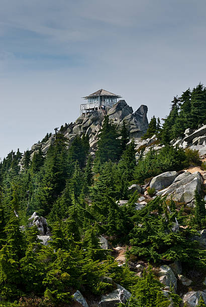 Mount Pilchuck Fire Lookout Mount Pilchuck State Park, Washington, USA - August 11, 2015: The historic Mount Pilchuck fire lookout was originally built in 1918 and rebuilt for visitor use in 1990. The lookout can be reached by hiking through beautiful old-growth forest and heather-covered meadows to the rocky summit. There you can see an incredible panoramic view of the Puget Sound lowlands and the Cascade and Olympic Mountains. These hikers were photographed standing on the fire lookout deck after reaching the 5341' summit of the mountain. Mount Pilchuck is near Granite Falls, Washington State, USA. jeff goulden fire lookout stock pictures, royalty-free photos & images