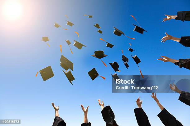 Happy Young Graduates Throwing Hats Stock Photo - Download Image Now - Graduation, Mortarboard, Sun