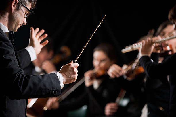 Conductor directing symphony orchestra Conductor directing symphony orchestra with performers on background. classical stock pictures, royalty-free photos & images