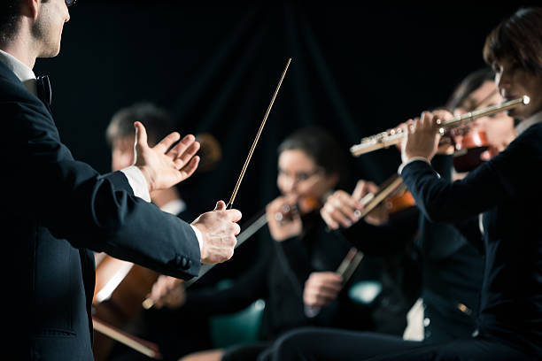 Conductor directing symphony orchestra Conductor directing symphony orchestra with performers on background. musical conductor photos stock pictures, royalty-free photos & images