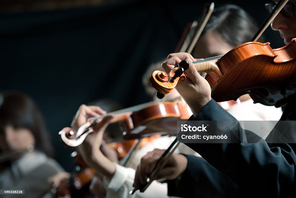 Symphony orchestra violinists performing Symphony orchestra violinists performing on stage against dark background. Violin Stock Photo