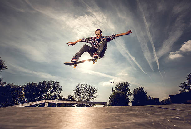 Low angle view of a young man skateboarding outdoors. Young extreme skateboarder practicing at the park against the sky. x games stock pictures, royalty-free photos & images