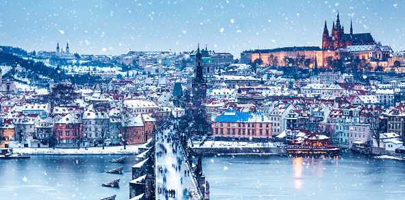 Prague (Czech Republic) with Charles bridge and St. Vitus chatedral on a snowy Christmas evening. People walking over the bridge.