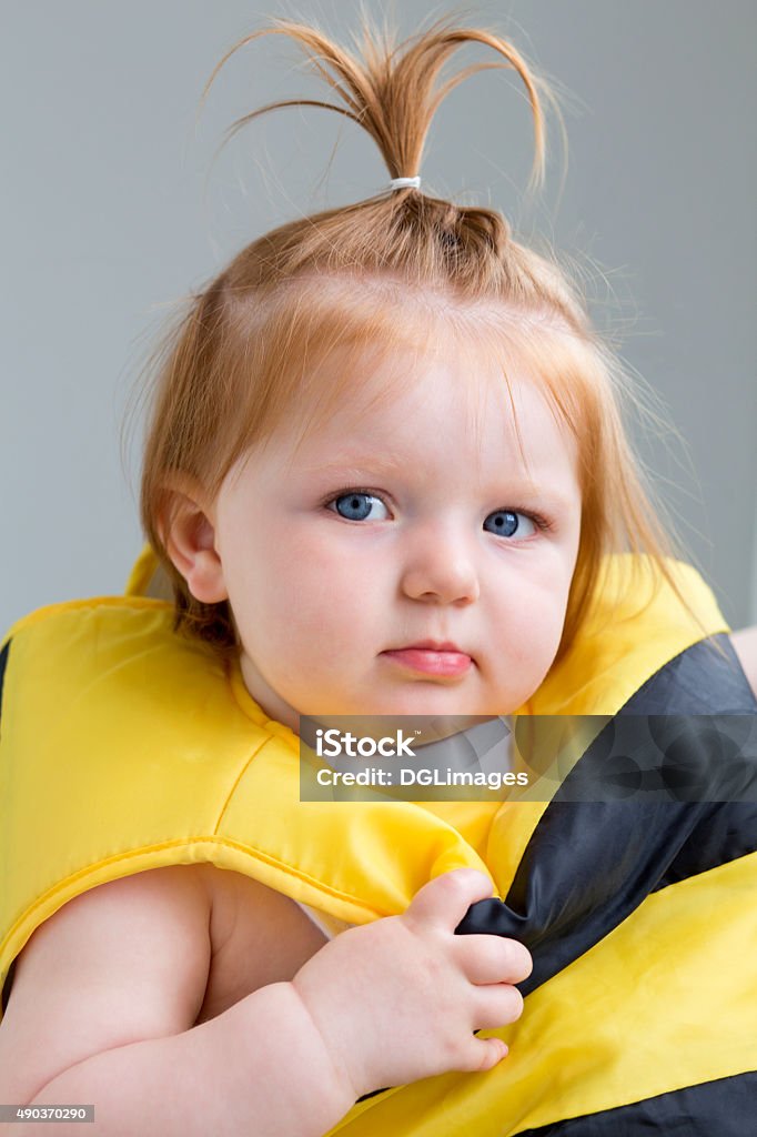 Bumble Bee Portrait of a baby girl in a bumble bee costume on a grey background. She is looking at the camera. 12-17 Months Stock Photo