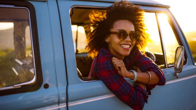 Woman in vintage car laughing at sunset