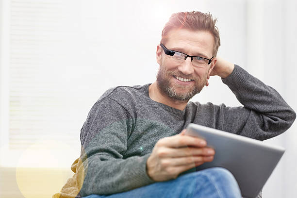 Young man wearing smart glasses with tablet at home Young man wearing smart glasses sitting at home with a digital tablet smiling smart glasses eyewear stock pictures, royalty-free photos & images