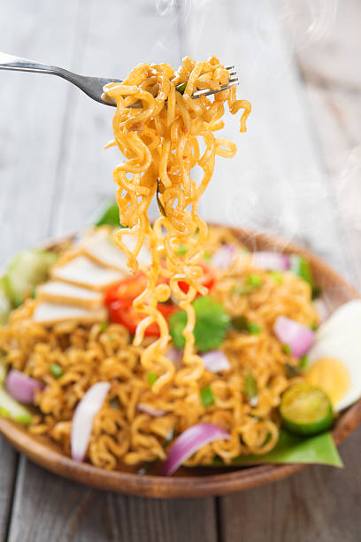 Spicy fried curry instant noodles or Malaysian style maggi goreng mamak.  Ready to serve on wooden dining table setting. Fresh hot with steamed smoke.