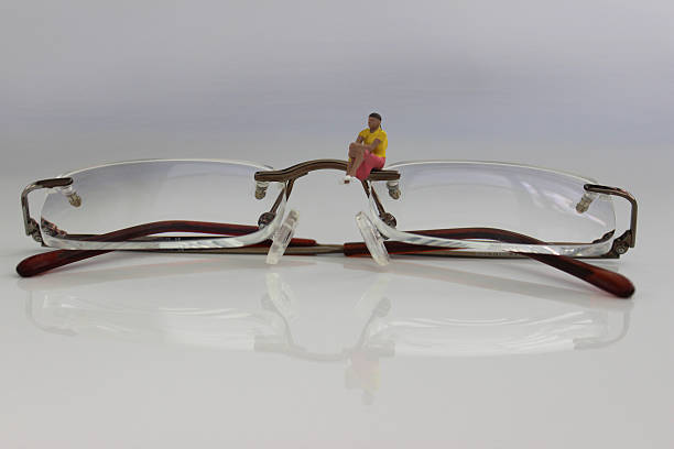 Frome, Somerset, England,UK - May, 6 2014: Photo depicting an eye health and optometry concept photo shot close-up in a studio setting showing a designer pair of rimless eye glasses from Dollond & Aitchison opticians. Sat on the lens is a female figure (using miniature figurines made by Preiser for model railways).