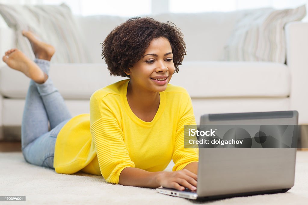 happy african american woman with laptop at home people, technology and leisure concept - happy african american young woman lying on floor with laptop computer at home Adult Stock Photo