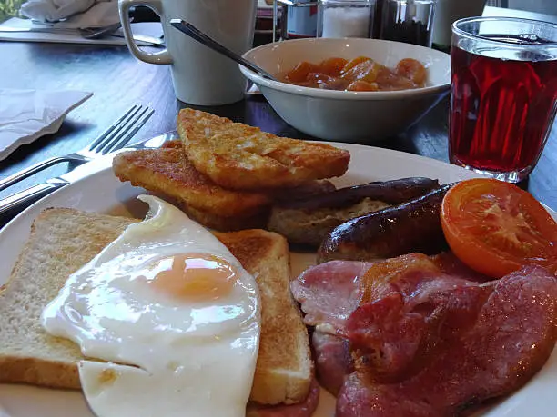 Photo showing some fried breakfast fry up food, including sausages, bacon, a fried egg, grilled tomatoes and some crispy white toast.