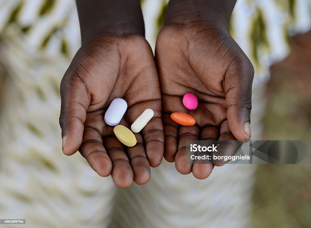 Healthy Lifestyle Medicine African Black Boy Holding Colorful Pills Background Medicine Healthcare Symbol. Black African boy holding pills to cure diseases. Unfortunately, in Africa there are lots of diseases like malaria, pneumonia, AIDS or simple Diarrhoea. Thereforem, medicine and healthcare pills are very important in the black continent. AIDS Stock Photo