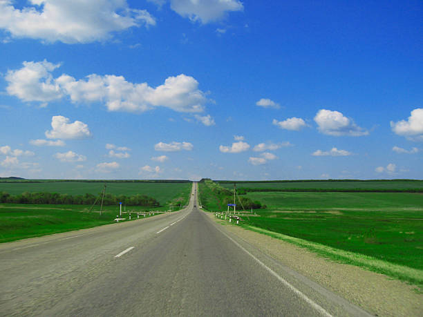 Wide highway and meadow. Clouds over and blue sky
