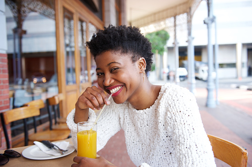 Close up portrait of a smiling black girl drinking orange juice at outdoor cafe