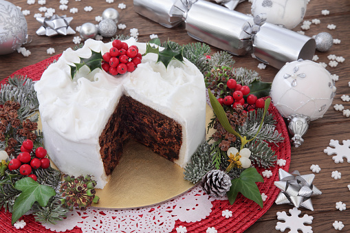 Traditional christmas cake with holly, bauble decorations and winter greenery over oak background.