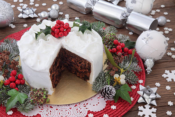 Traditional Christmas Cake Traditional christmas cake with holly, bauble decorations and winter greenery over oak background. christmas cake stock pictures, royalty-free photos & images