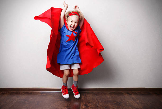 Happy child in superhero suit against gray wall.
