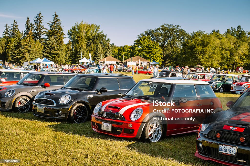 Red Mini Cooper S JCW at the Car Show Burlington, Ontario, Canada- September 20, 2015. Line up of  Mini Cooper small vehicles parked on the field at public park in Burlington, Ontario as a part of the "British Car Day" show, the largest North American British made car gathering. Numerous show visitors in the background, checking out other vehicles on display. British Car Day is hosted annually by the Toronto Triumph Club, on the third Sunday of September. Since its inaugural event in 1984, it has grown in leaps and bounds, and now draws over 1,000 British cars and 8,000 spectators. British Car Day is open to vintage, classic and current British manufactured vehicles, including motorcycles.  2015 Stock Photo