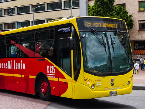 Bogotá, Colombia - September 24, 2015: The front section of a TransMilenio articulated bus in downtown Bogota, the capital city of Colombia in South America.  Some passengers can be seen in the bus; and a few people on the sidewalk. In the background is an office building. Photo shot in the afternoon sunlight; horizontal format.