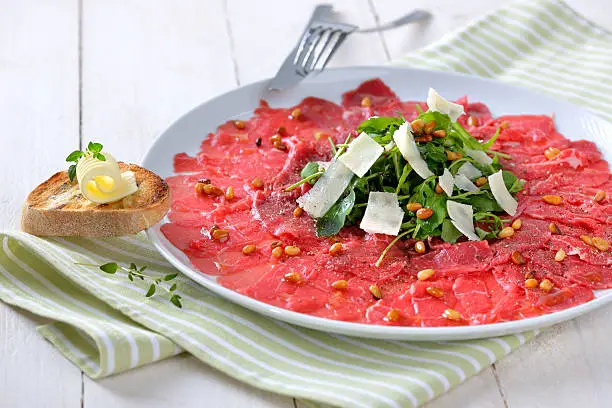 Carpaccio of beef fillet with rocket salad, parmesan cheese and roasted pine nuts, served with a slice of toasted baguette with a butter roll