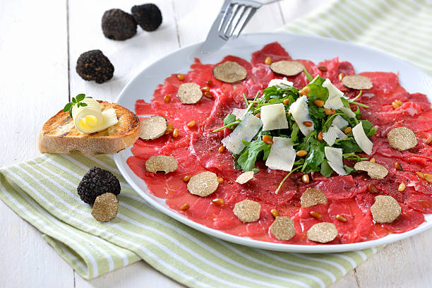 Carpaccio with truffles Carpaccio of beef fillet with sliced black truffles, rocket salad with parmesan cheese and roasted pine nuts, served with a slice of toasted baguette with a butter roll tartuffo stock pictures, royalty-free photos & images