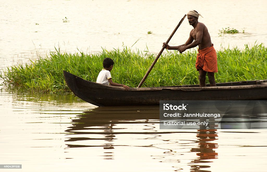 Kerala, India: Fisherman, Child, and Canoe in Kerala Backwaters Kottayam (Kerala), India - November 24, 2009: A fisherman standing and poling in his traditional canoe in a lagoon in the Southern Kerala backwaters at dusk. A child is sitting in the boat. Malabar Coast Stock Photo