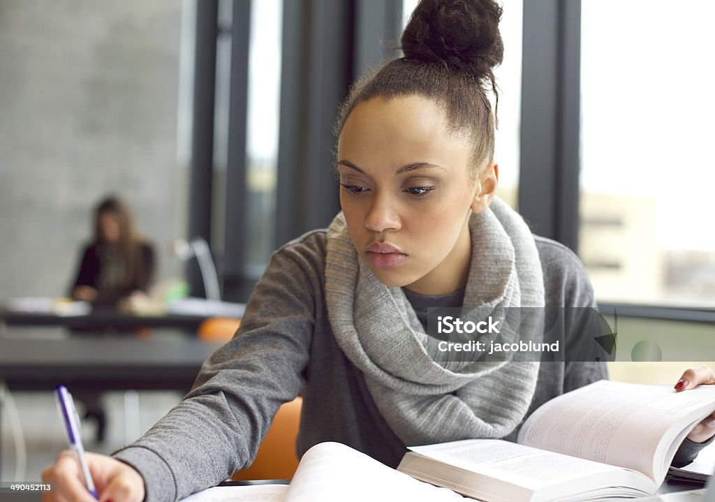 Young afro american woman doing assignments in library Close up image of a young female student doing assignments in library. Afro american woman taking notes from textbooks. Studying Stock Photo
