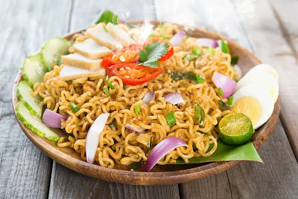 Malaysian style maggi goreng mamak  or spicy fried curry instant noodles.  Asian cuisine, ready to serve on wooden dining table setting. Fresh hot with steamed smoke.